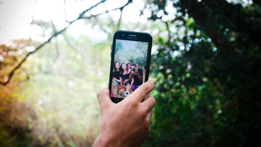 A photograph of a selfie being taken, showing people in a forest