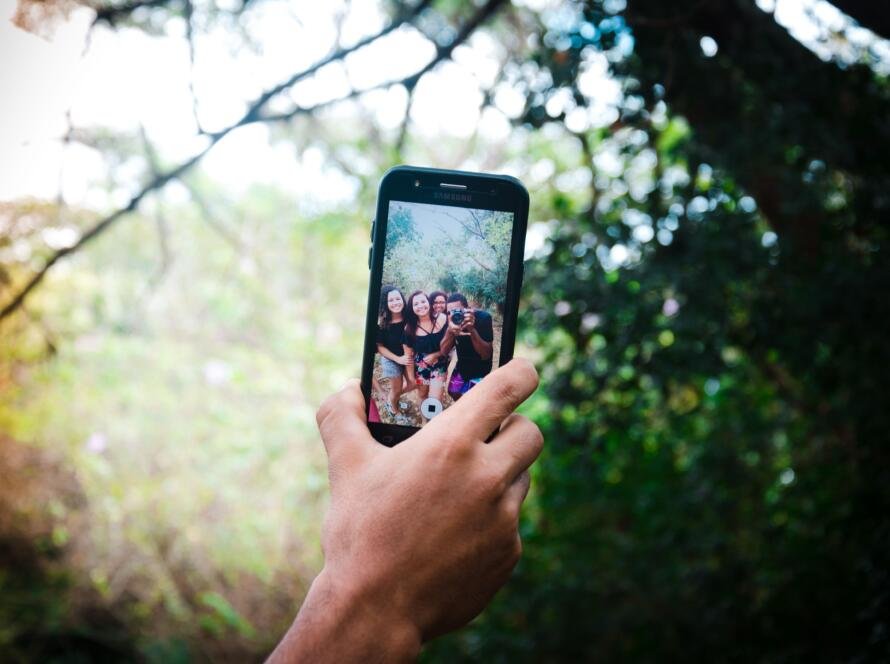 A photograph of a selfie being taken, showing people in a forest