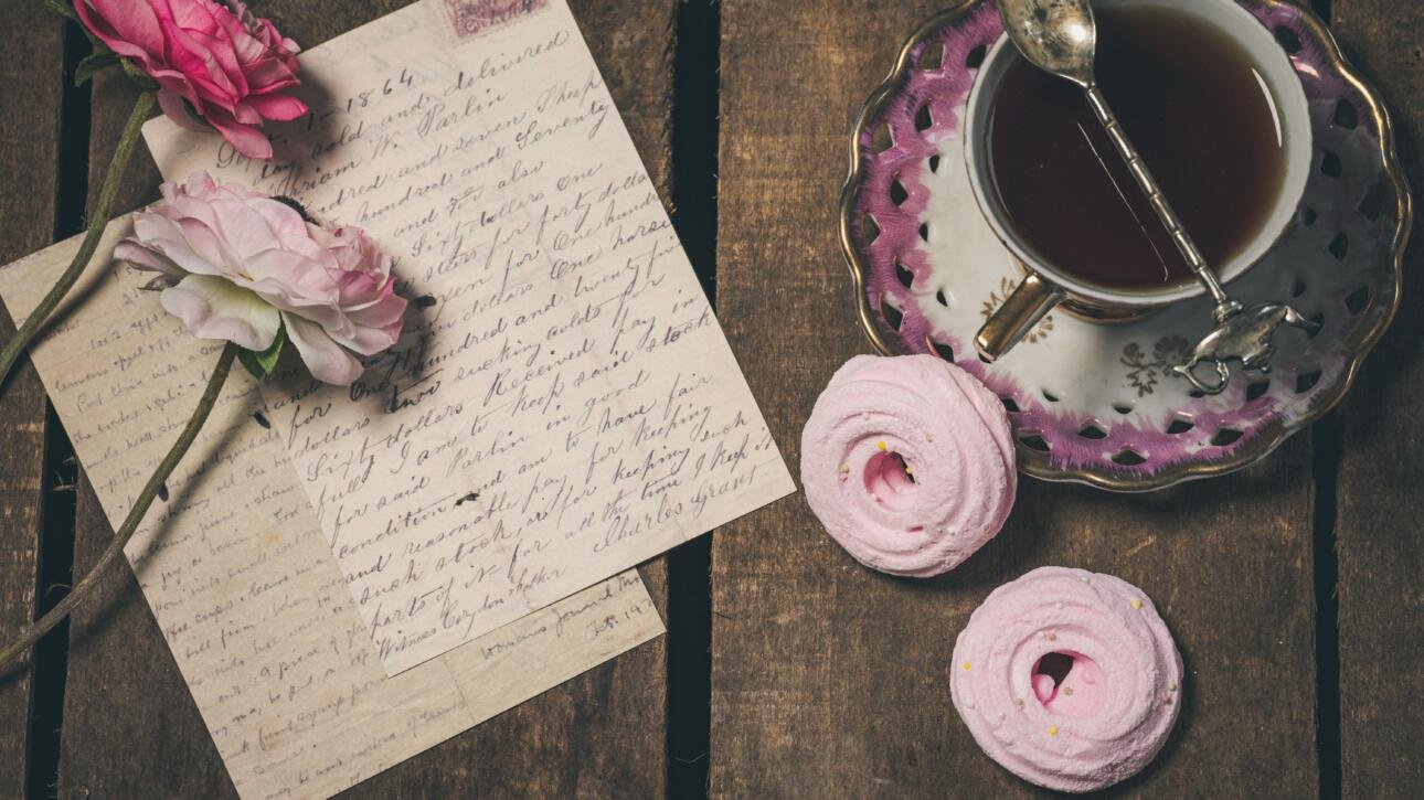 Handwritten letter, with flowers on it, next to a cup of tea