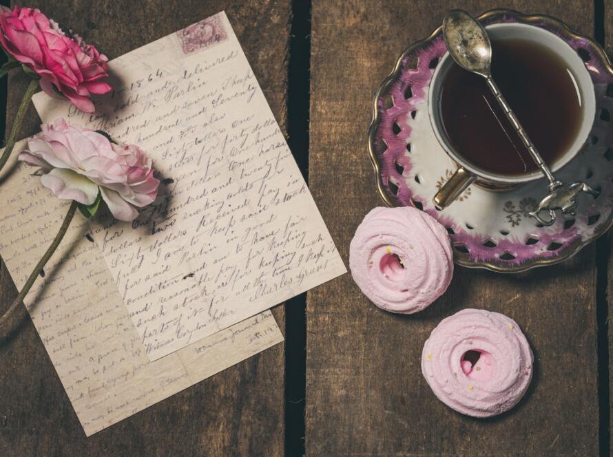 Handwritten letter, with flowers on it, next to a cup of tea